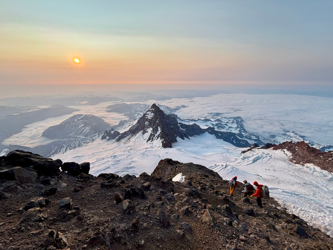 Two climbers on a mountain peak with a breathtaking view of snow-covered landscape and sunset.