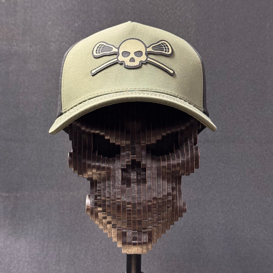 Front view of the loden and black Skull & Sticks Lacrosse Hat on a wooden skull display.